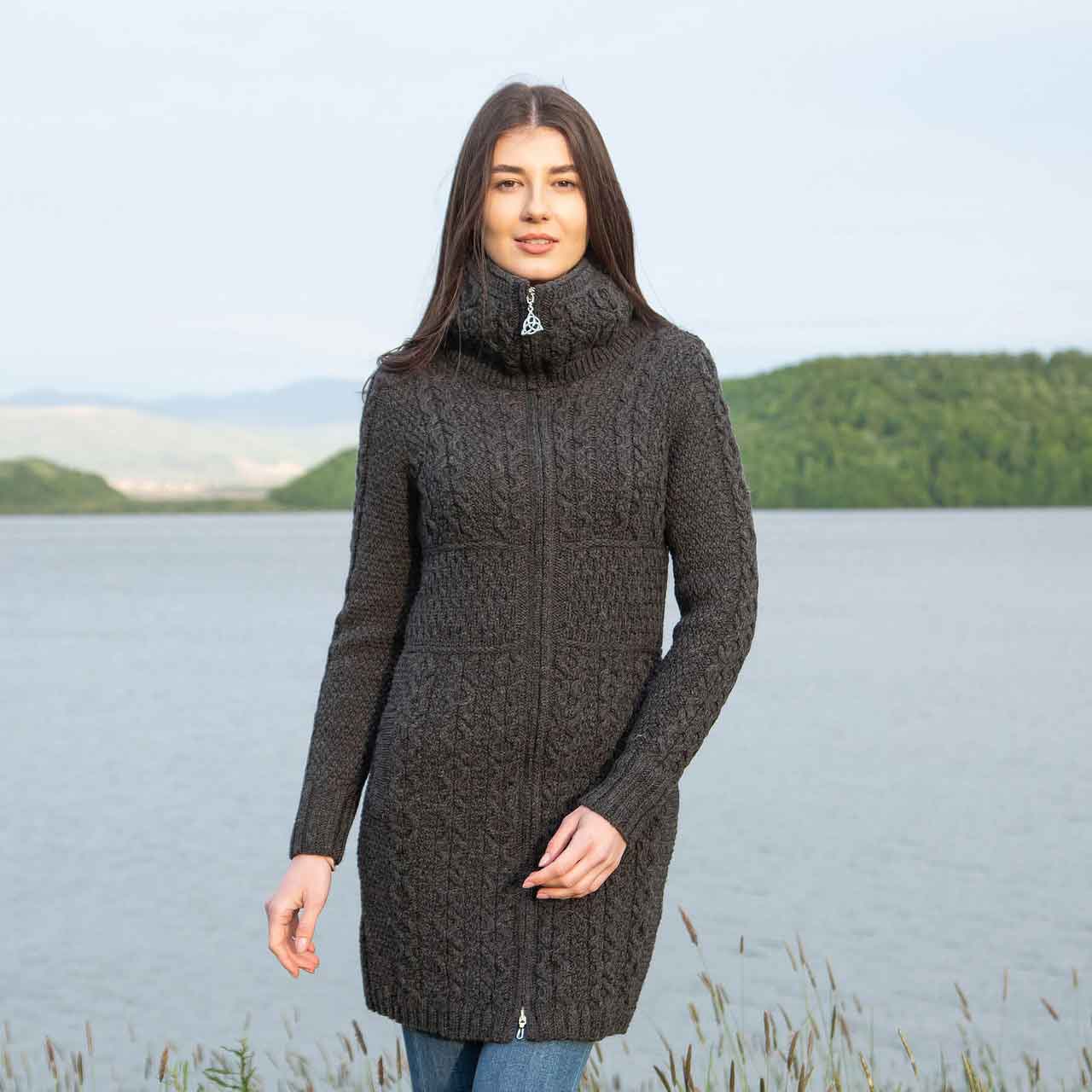 woman wearing a charcoal irish aran double collar zip ladies cardigan knitted coat standing by a lake with green hills in the background