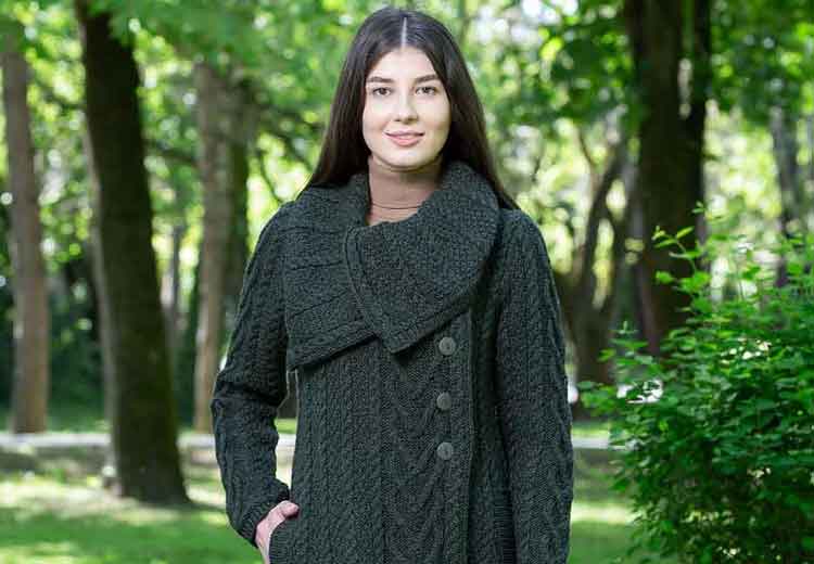 Woman modelling a dark green aran knit coat in a forest