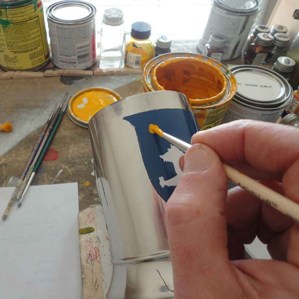close up of our artist hand painting a coat of arms tankard