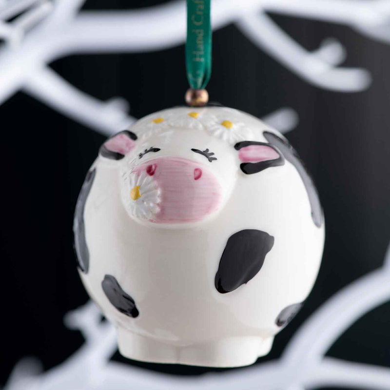 Belleek Daisy the Cow Ornament - A white cow-shaped ornament with black spots hanging against a black background