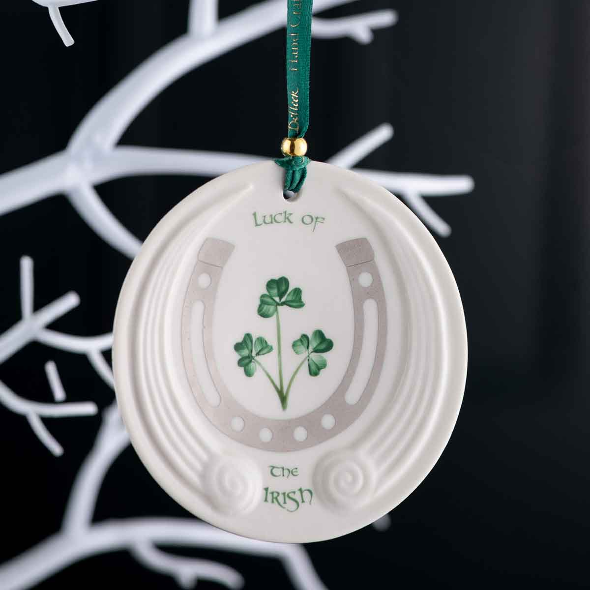 belleek luck of the irish ornament - an oval decorative ornament with shamrock design, horseshoe and and text reading luck of the irish hanging on a christmas tree