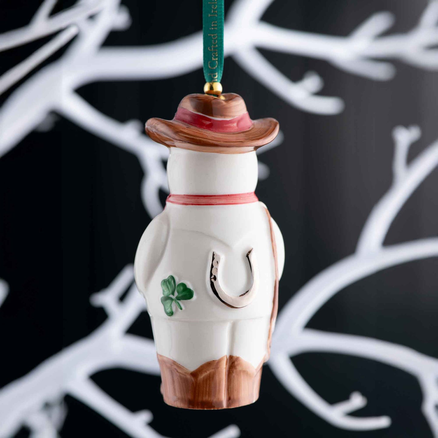 belleek wild west snowman ornament. view of the reverse of the snowman ornament with a hat, shamrock, and horseshoe on a black background.