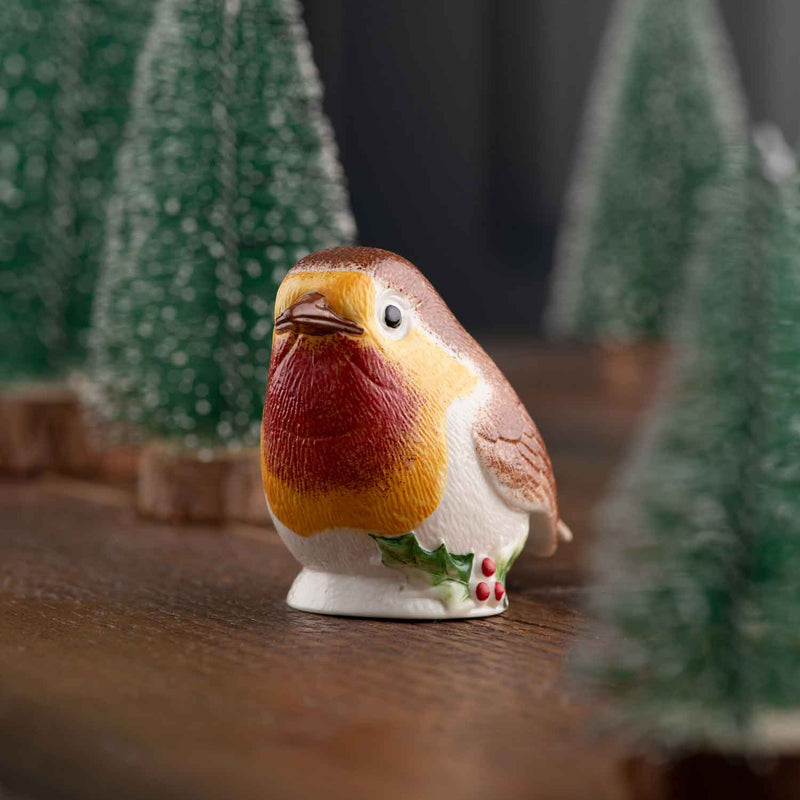 Belleek Robin with Holly Ornament - A ceramic ornament of a robin surrounded by fir trees standing on a wooden surface