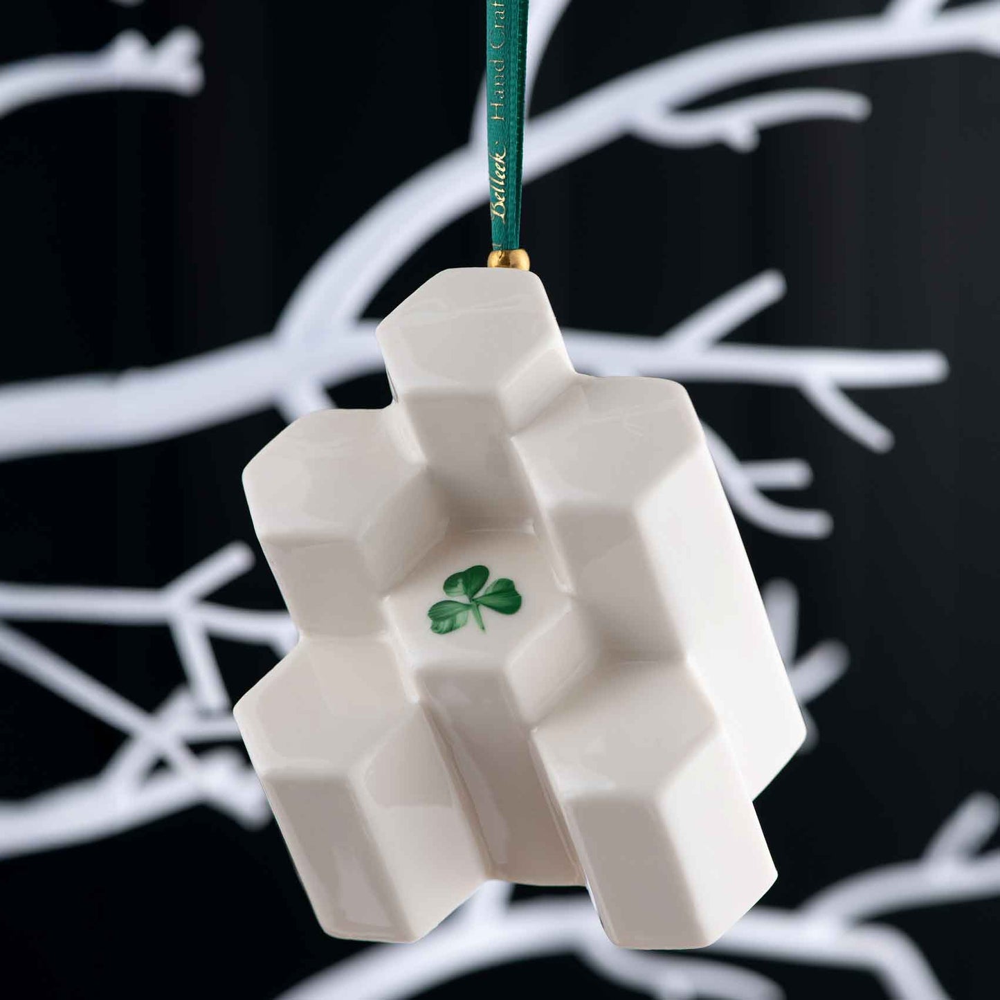 giants causeway belleek annual ornament 2025 - a decorative ornament in style of hexagonal basalt columns with green shamrock at its center hanging on a white branch against a black background