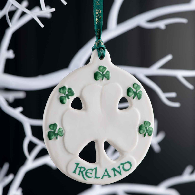 Belleek Ireland Shamrock Ornament A decorative ornament with an embossed shamrock design, handpainted shamrocks and 'Ireland' text, hanging on a white branch against a background.