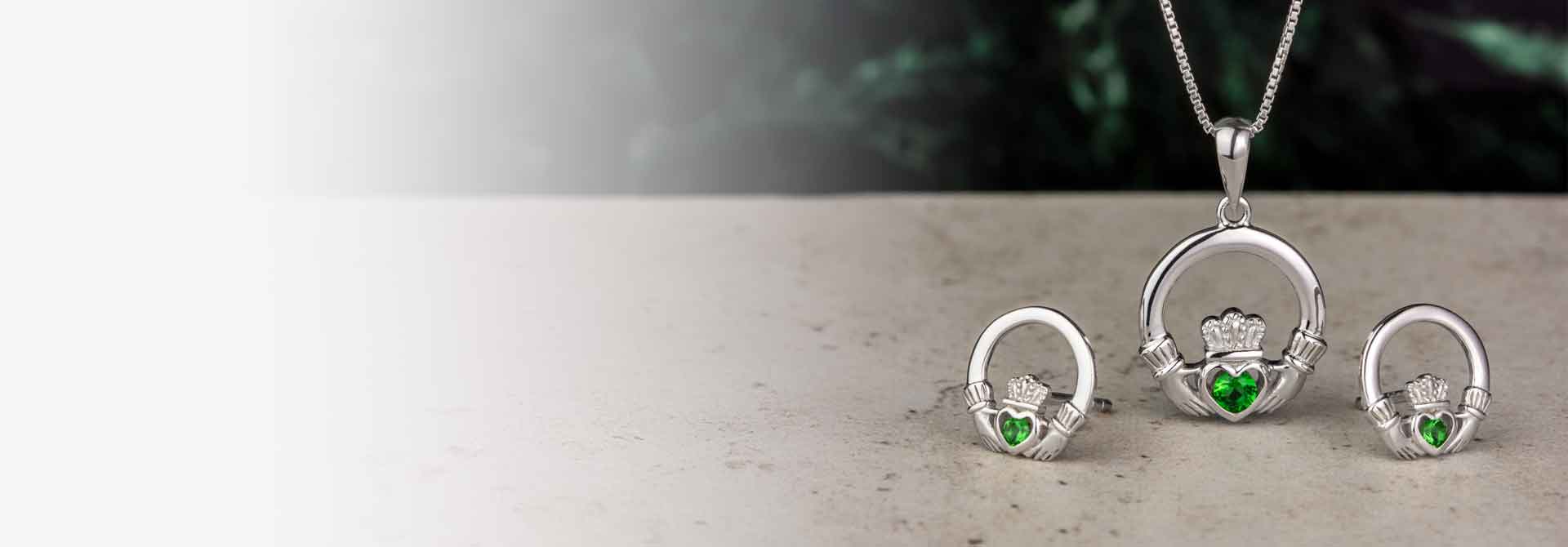 Silver Claddagh Necklace and Earings with a green crystal heart on a grey surface with green marble background