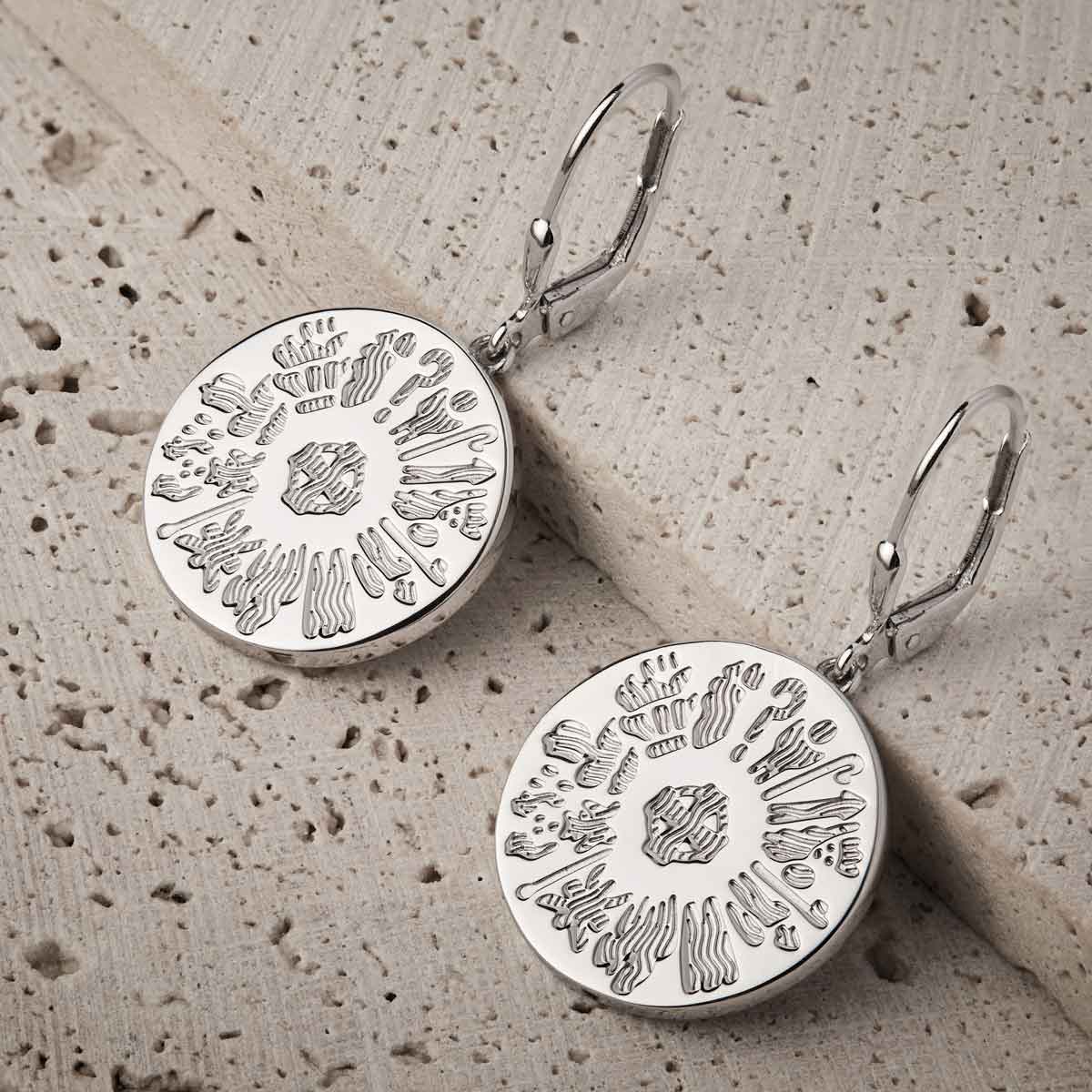 pair of sterling silver history of ireland disc earrings on a textured beige surface