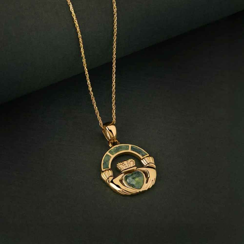 irish necklace - a 14k gold connemara marble claddagh pendant against a dark green fabric background