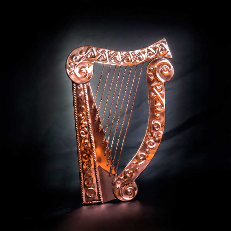 decorative copper harp plaque with embossed celtic detail against a dark background
