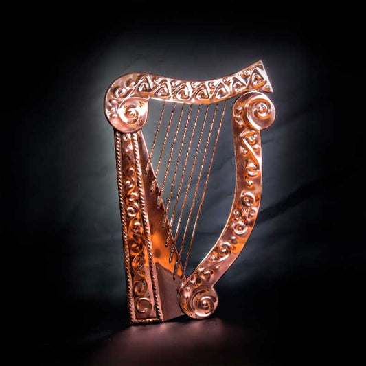Decorative copper harp plaque with embossed celtic detail against a dark background