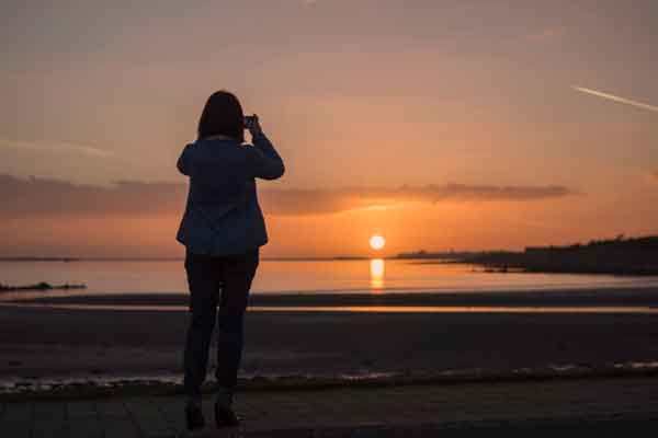 Silhouette of woman taking a photo of sunset over Galway Bay