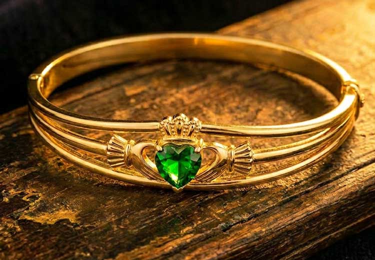 A Gold Plated Green Crystal Heart Claddagh Bangle on a wooden surfaceresting on a rustic wooden surface.