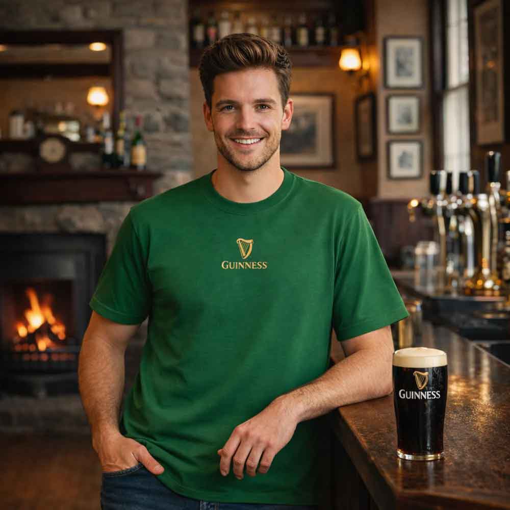 man wearing a guinness® are you toucan to me green t-shirt in a bar setting with a pint of guinness on the counter.