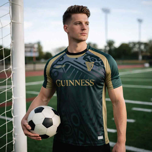 Man holding a soccer ball on a sports field wearing a Guinness® Retro Harp Performance Soccer Jersey