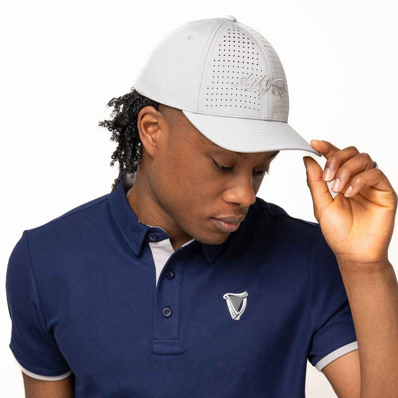 Man wearing a Guinness® White Performance Signature Baseball Cap and blue polo shirt on a white background