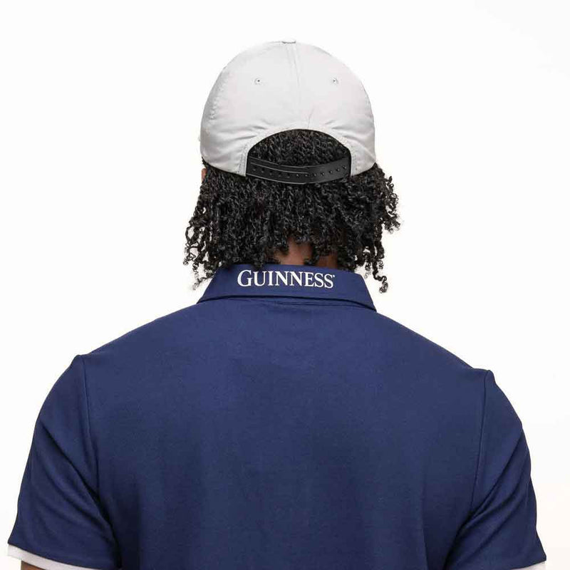Person wearing a blue polo shirt with 'Guinness' branding on the back, and a Guinness® White Performance Signature Baseball Cap on his head