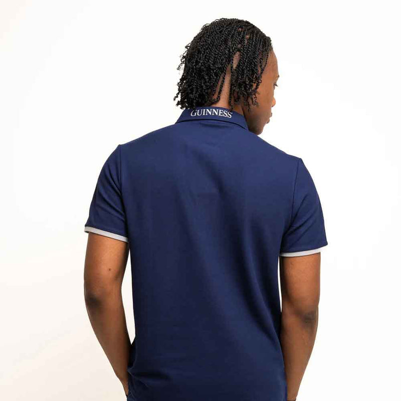Person wearing a Guinness® Navy Performance Polo Shirt with 'Guinness' branding embroidered on the collar, on a white background