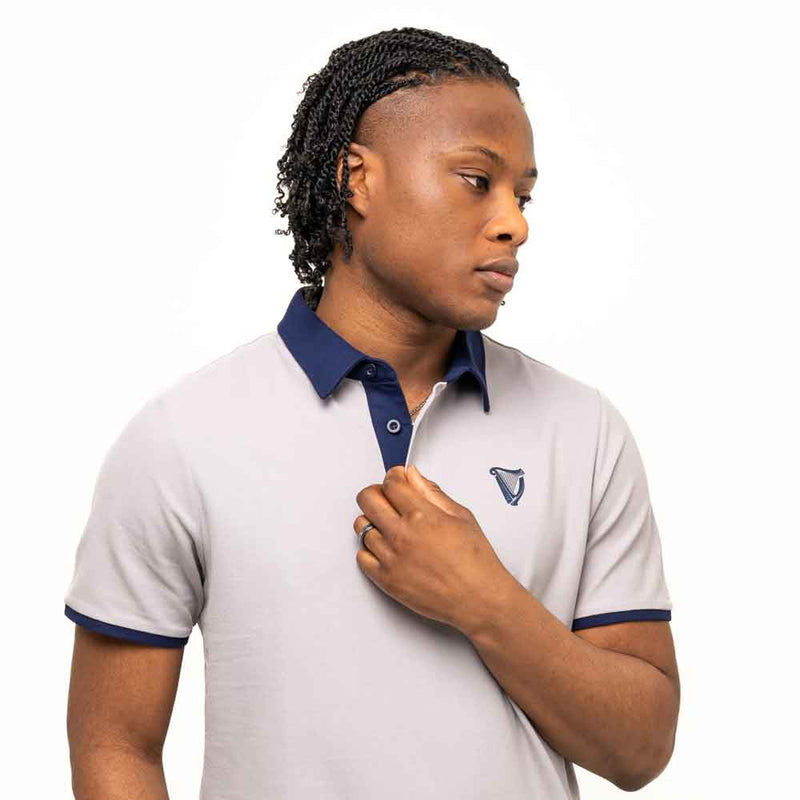 Man wearing a Guinness® Gray Performance Polo Shirt, with their hand on their chest, on a white background