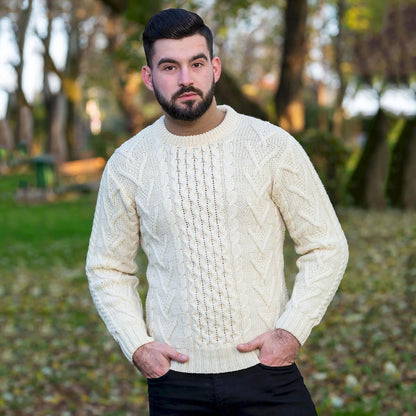 A man wearing a natural-colored Merino Wool Classic Aran Knit Men's Sweater in outdoors with trees in the background