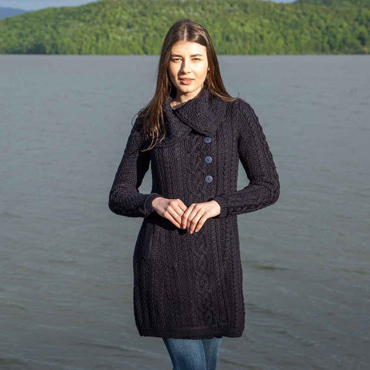 Woman wearing a navy Irish Aran Knit four button collar cardigan coat standing by a lake with mountains in the background
