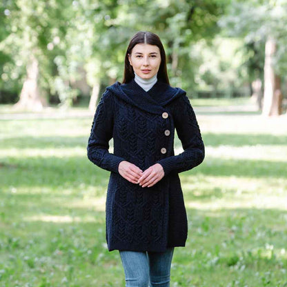 A woman wearing a Navy Ladies Aran Leaf Cable Knit Coat in an outdoor, parkland setting