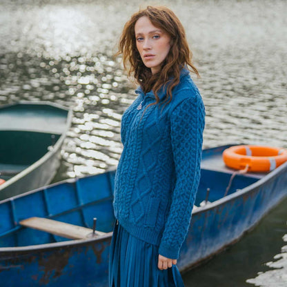A woman stands in a blue rowboat on a lake, wearing an Teal Ladies Cable Knit Bomber Jacket and blue skirt. Another blue boat and an orange life preserver are visible in the background.