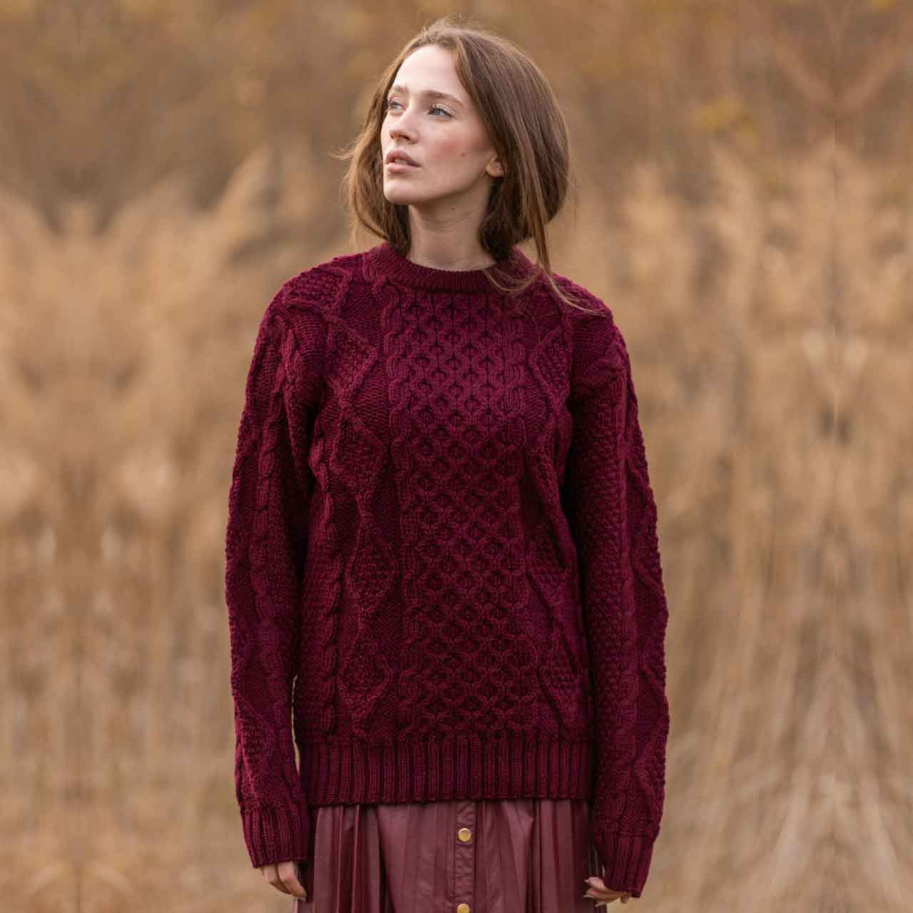  woman wearing a wine colored fisherman cable knit ladies sweater  against a blurred natural background