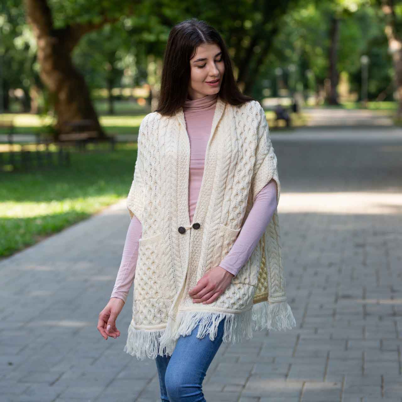 woman wearing a white/natural aran knit ladies pocket shawl in a park setting