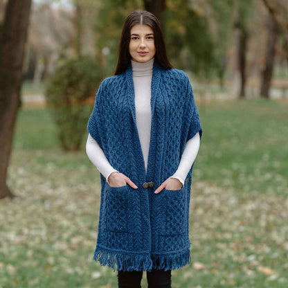 Woman wearing a teal Aran Knit Ladies Pocket Shawl in a park setting