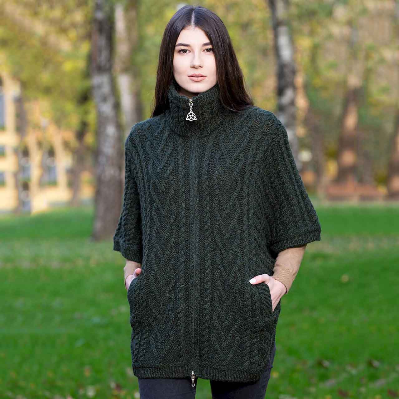 woman wearing an aran knit funnel neck poncho jacket in army green in a park setting