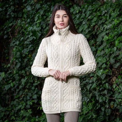 Woman wearing a white/natural Irish soft-merino Aran knit ladies zip cardigan standing in front of an ivy covered wall