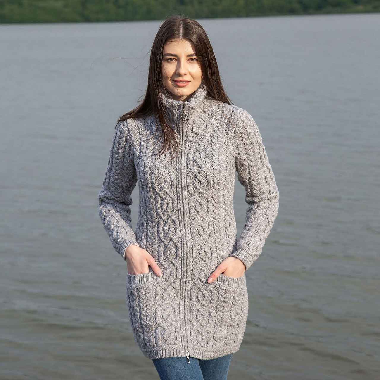 woman wearing a grey irish soft-merino aran knit ladies zip cardigan standing by a lake with mountains in the background