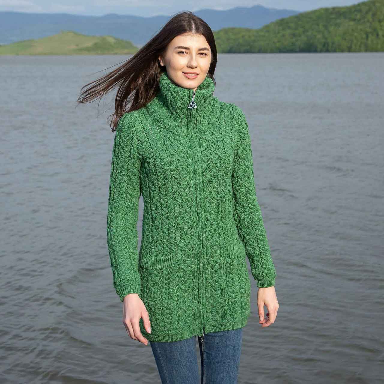 woman wearing a green irish soft-merino aran knit ladies zip cardigan standing by a lake with mountains in the background