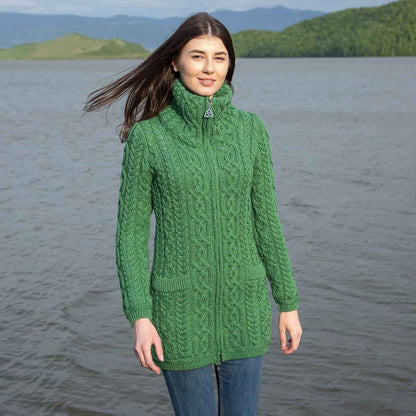 Woman wearing a green Irish soft-merino Aran knit ladies zip cardigan standing by a lake with mountains in the background