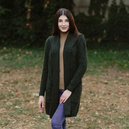 Woman wearing an army green Aran Knit Hooded Ladies Long Cardigan in an outdoor setting with trees and grass.