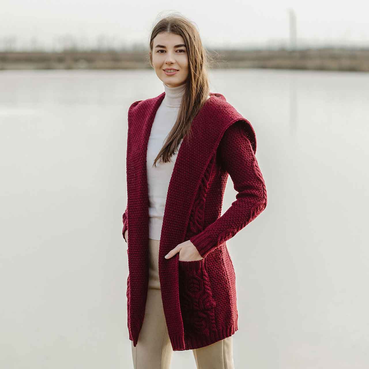 woman wearing a wine aran knit hooded ladies long cardigan in front of a lake 