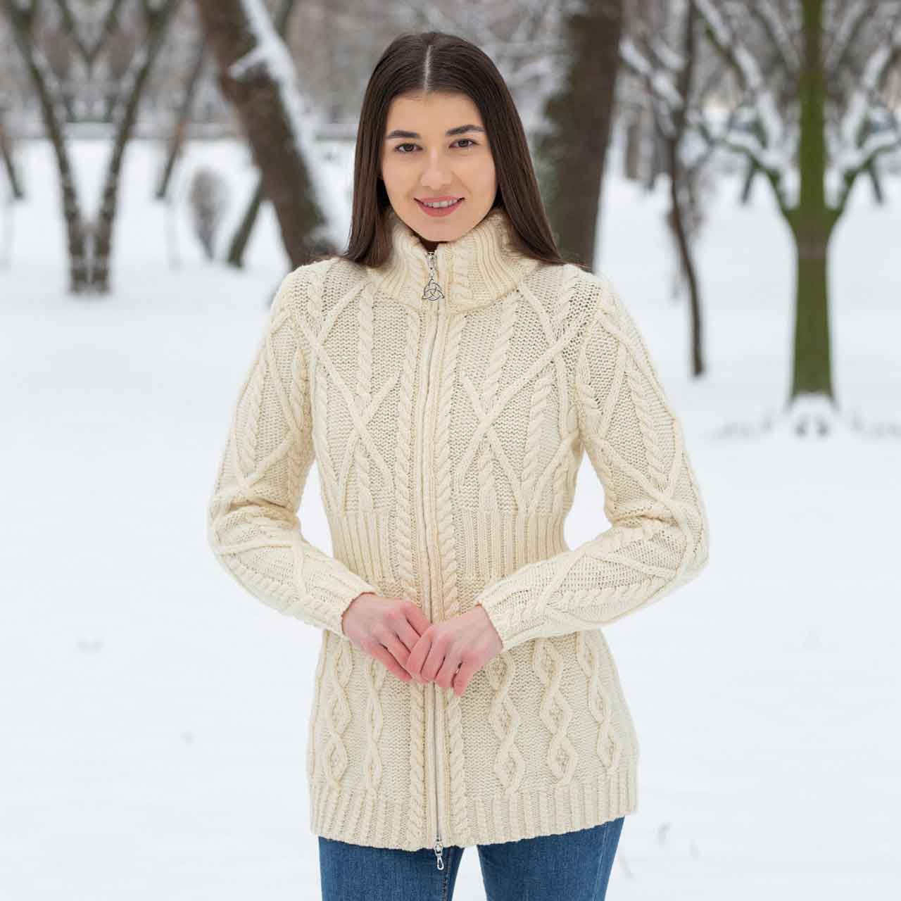 woman wearing a natural/white colored soft touch merino aran knit ladies zip cardigan in a snowy landscape