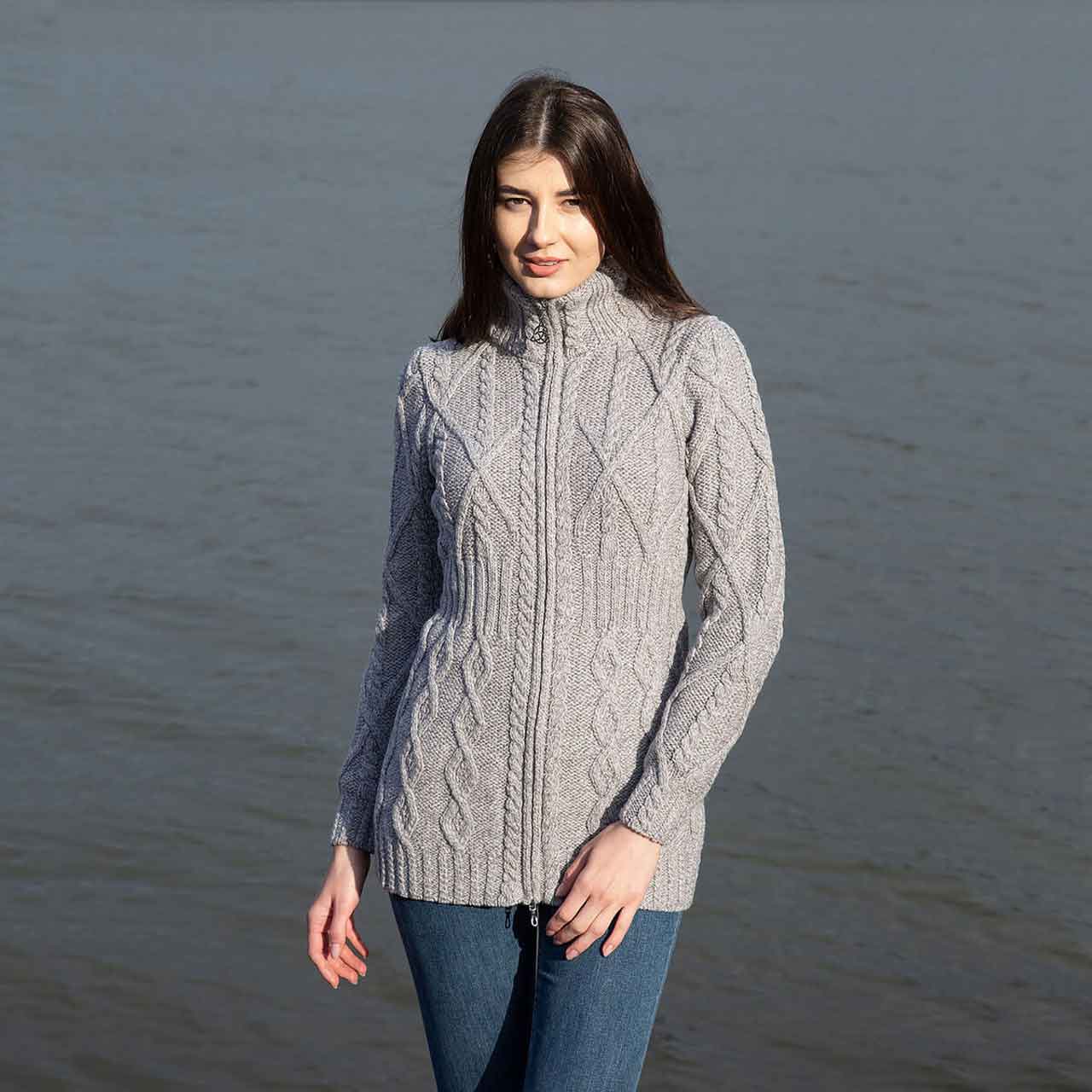 woman wearing a gray soft touch merino aran knit ladies zip cardigan standing by a body of water.