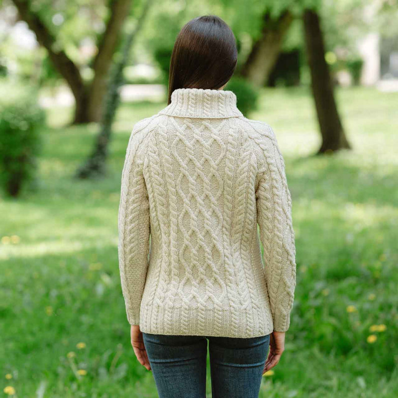 Reverse view of a woman wearing a parsnip-colored Irish Aran ladies merino wool zipper neck sweater in a park setting