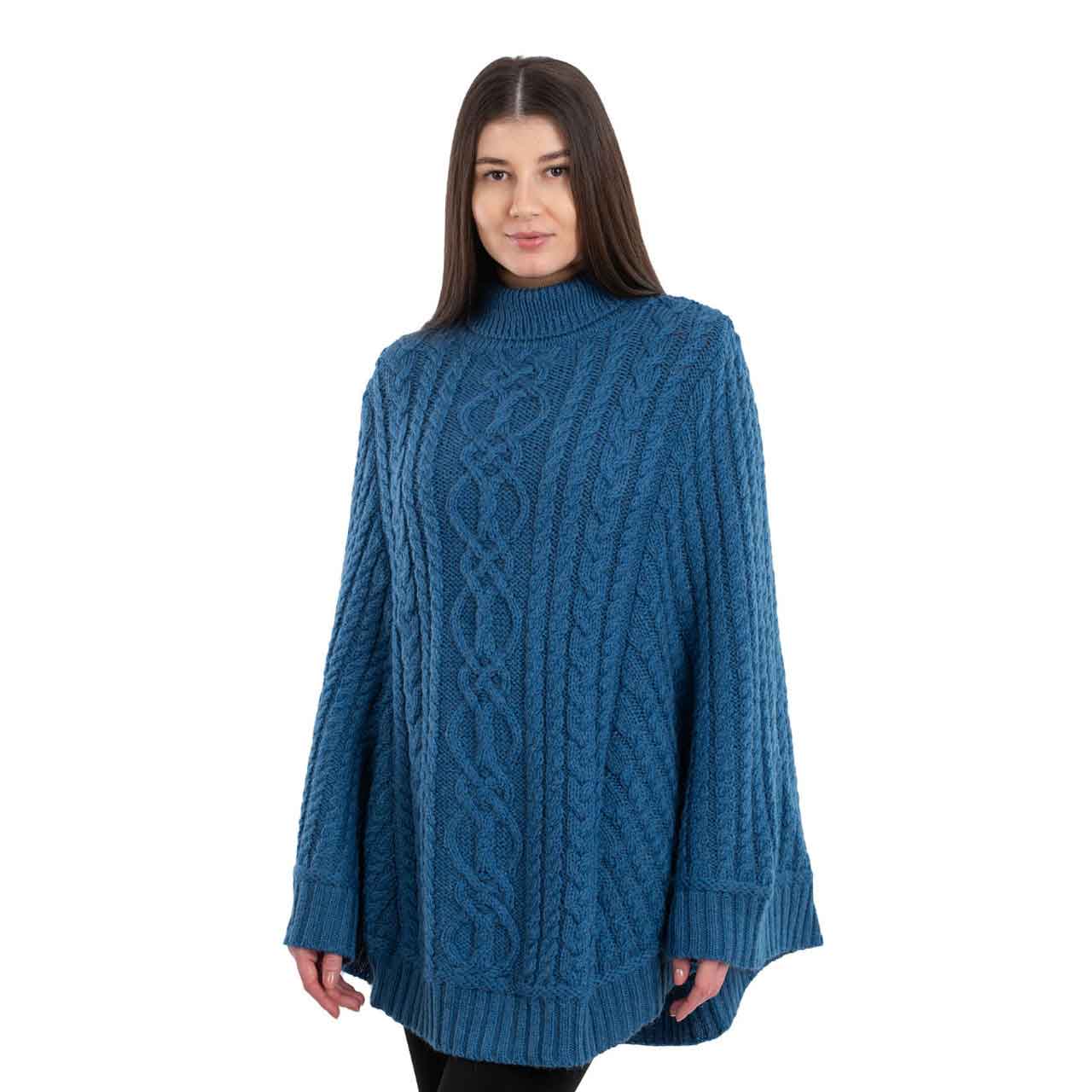 woman wearing a teal aran cable knit poncho on a white background