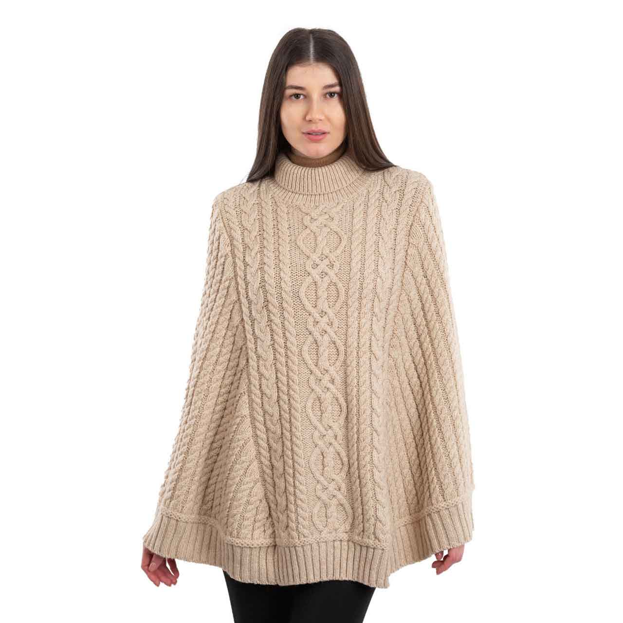 woman wearing a parsnip colored aran cable knit poncho on a white background