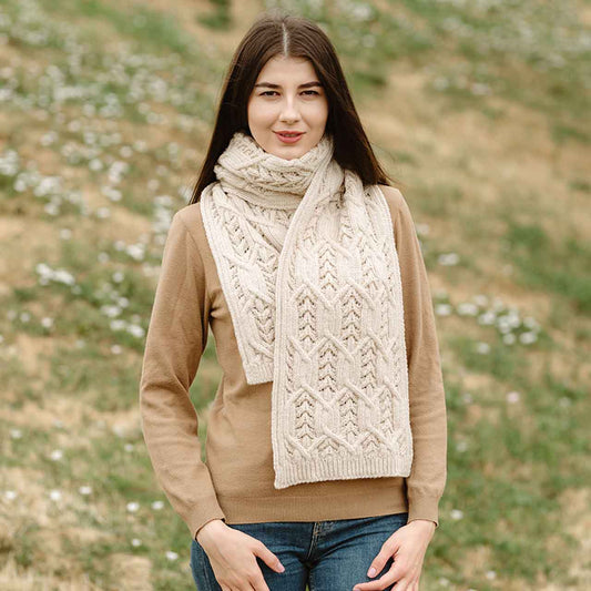 Woman wearing a beige sweater and natural colored Merino wool Aran Knit Leaf Ladies Scarf scarf standing in a field with wildflowers.