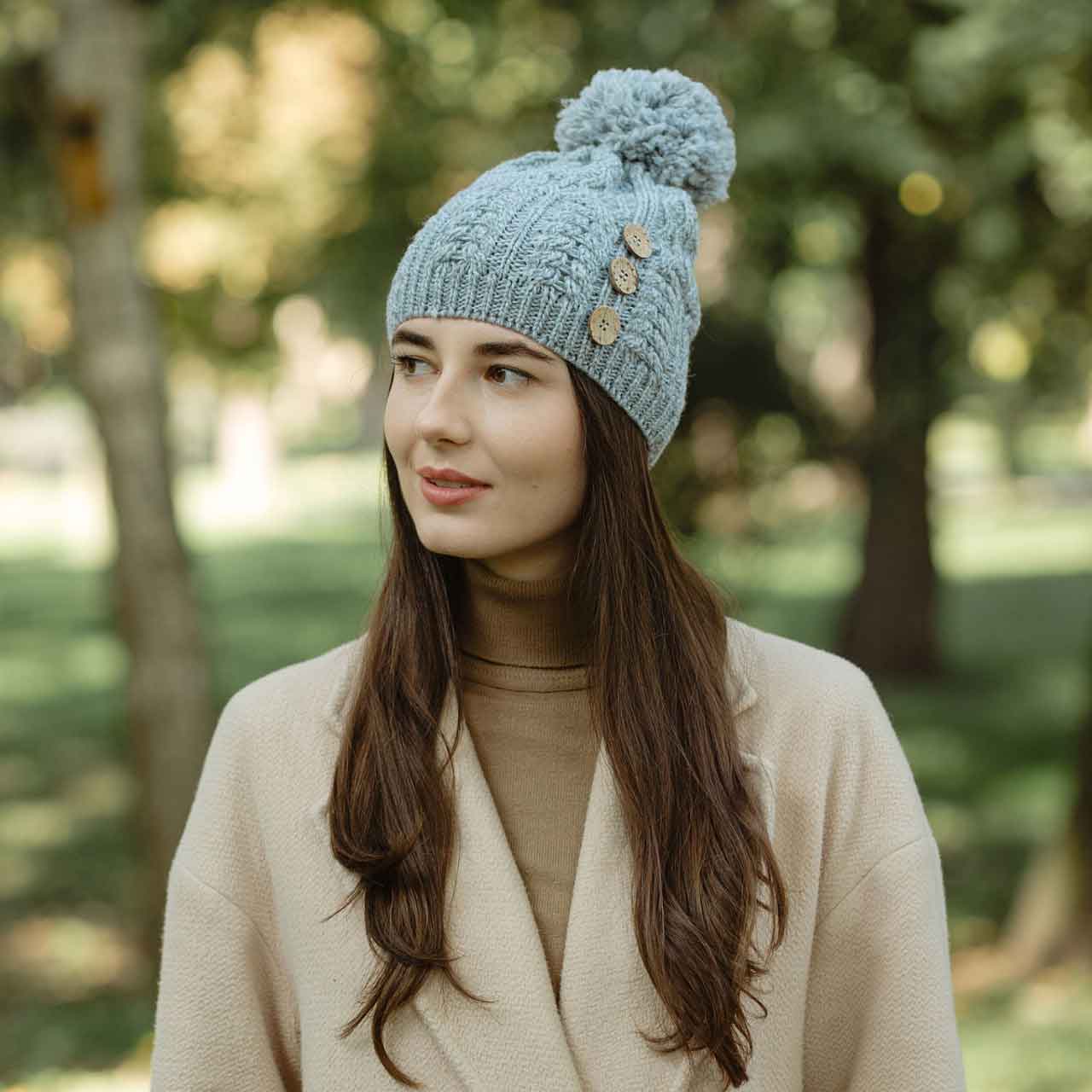 woman wearing a gray colored merino anan knit button pom-pom hat standing in a park