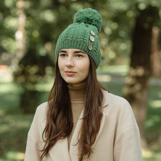 Woman wearing a green colored merino Anan Knit button pom-pom hat standing in a park