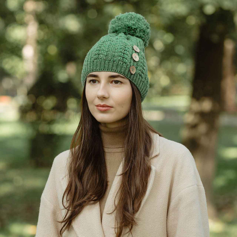 Woman wearing a green colored merino Anan Knit button pom-pom hat standing in a park