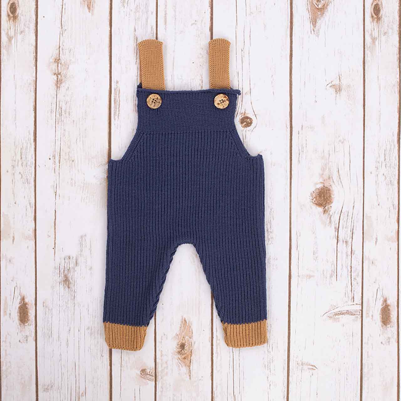 navy blue irish baby knitted romper overalls with brown cuffs and buttons on a wooden background