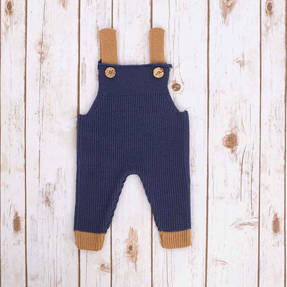 Navy blue Irish baby knitted romper overalls with brown cuffs and buttons on a wooden background