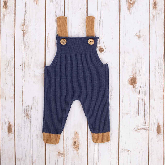 Navy blue Irish baby knitted romper overalls with brown cuffs and buttons on a wooden background