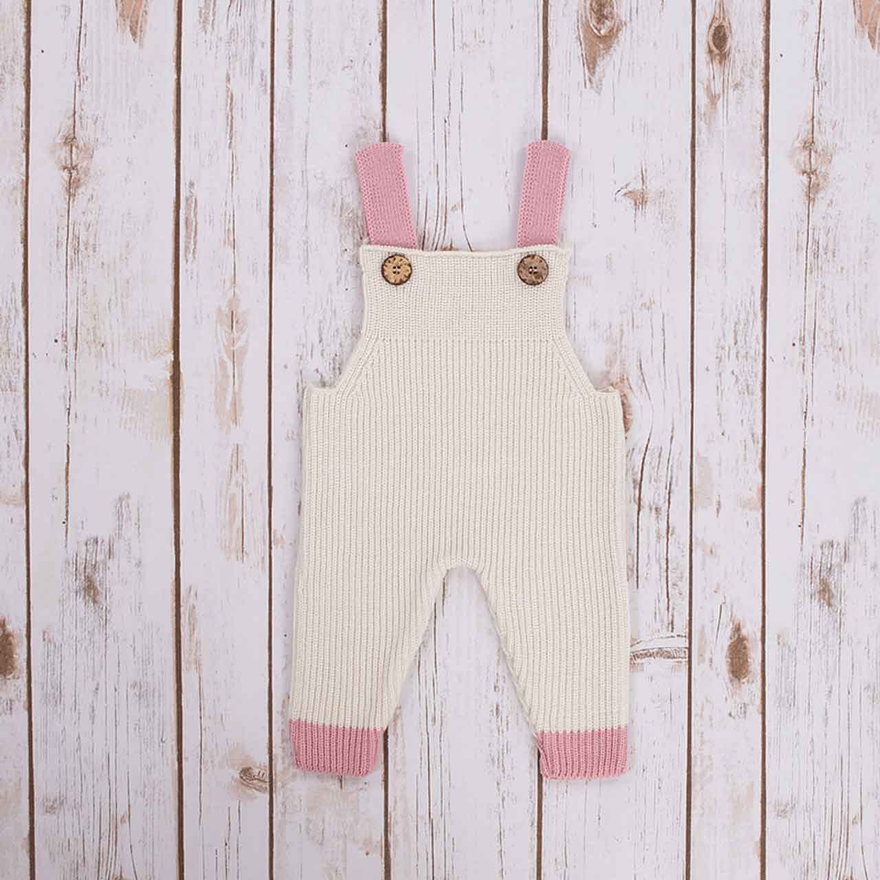white irish baby knitted romper overalls with pink cuffs and buttons on a wooden background
