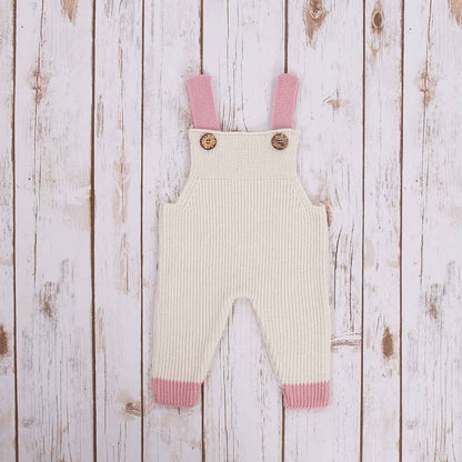 White Irish baby knitted romper overalls with pink cuffs and buttons on a wooden background
